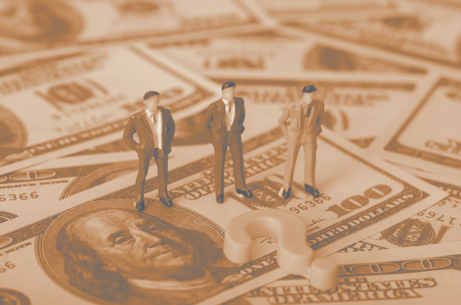 Three miniature businessman figurines standing on spread-out hundred dollar bills with a question mark