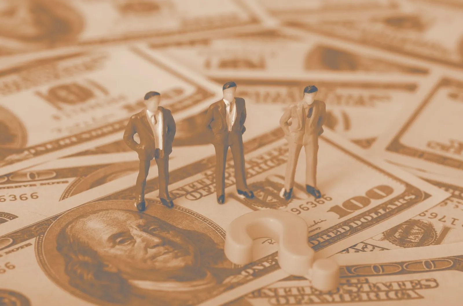 Three miniature businessman figurines standing on spread-out hundred dollar bills with a question mark
